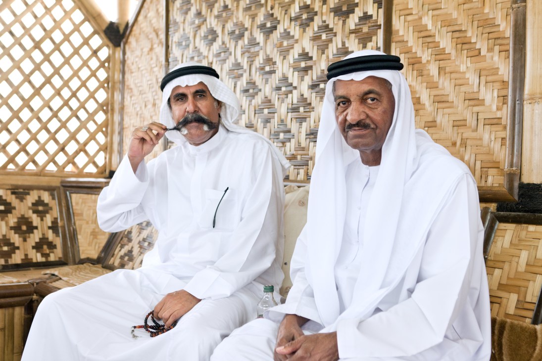 Two men in white traditional Gulf dress sit inside a hut with woven palm walls at Fujairah's corniche.