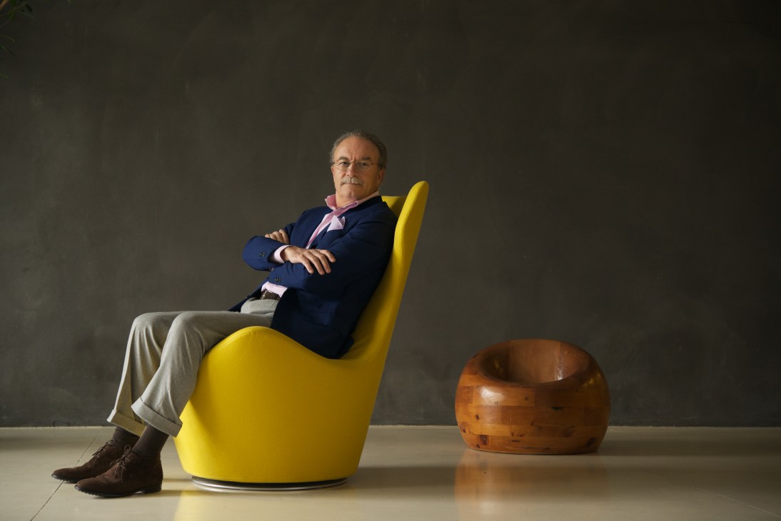 B&B Italia president Giorgio Busnelli sits in a yellow chair wearing a navy blazer and pink scarf.