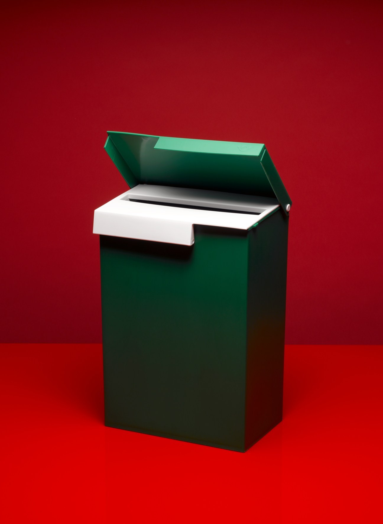 Green steel post box by Frost Produkt with white mail slot and self-locking lid against red background.