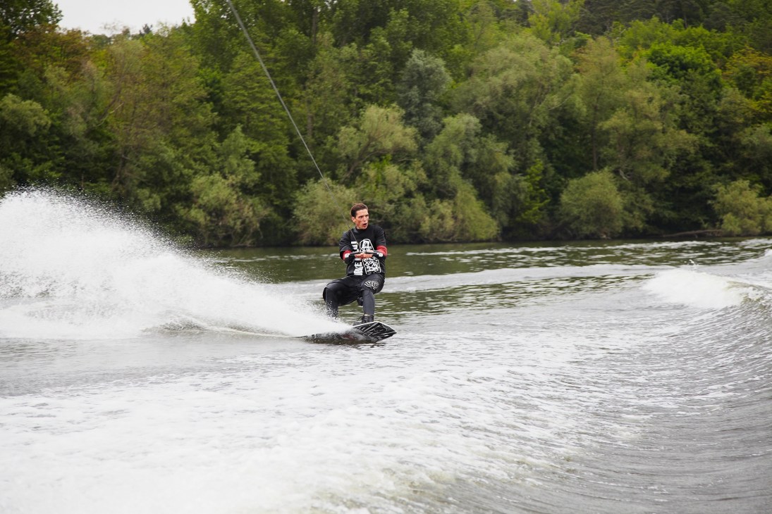 Man wakeboarding on a river with forested banks in the background.