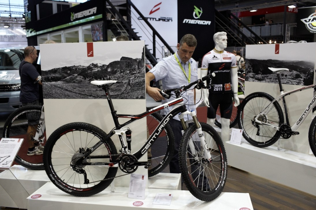 A man examines a Centurion Numinis Carbon LTD mountain bike at a trade show display.