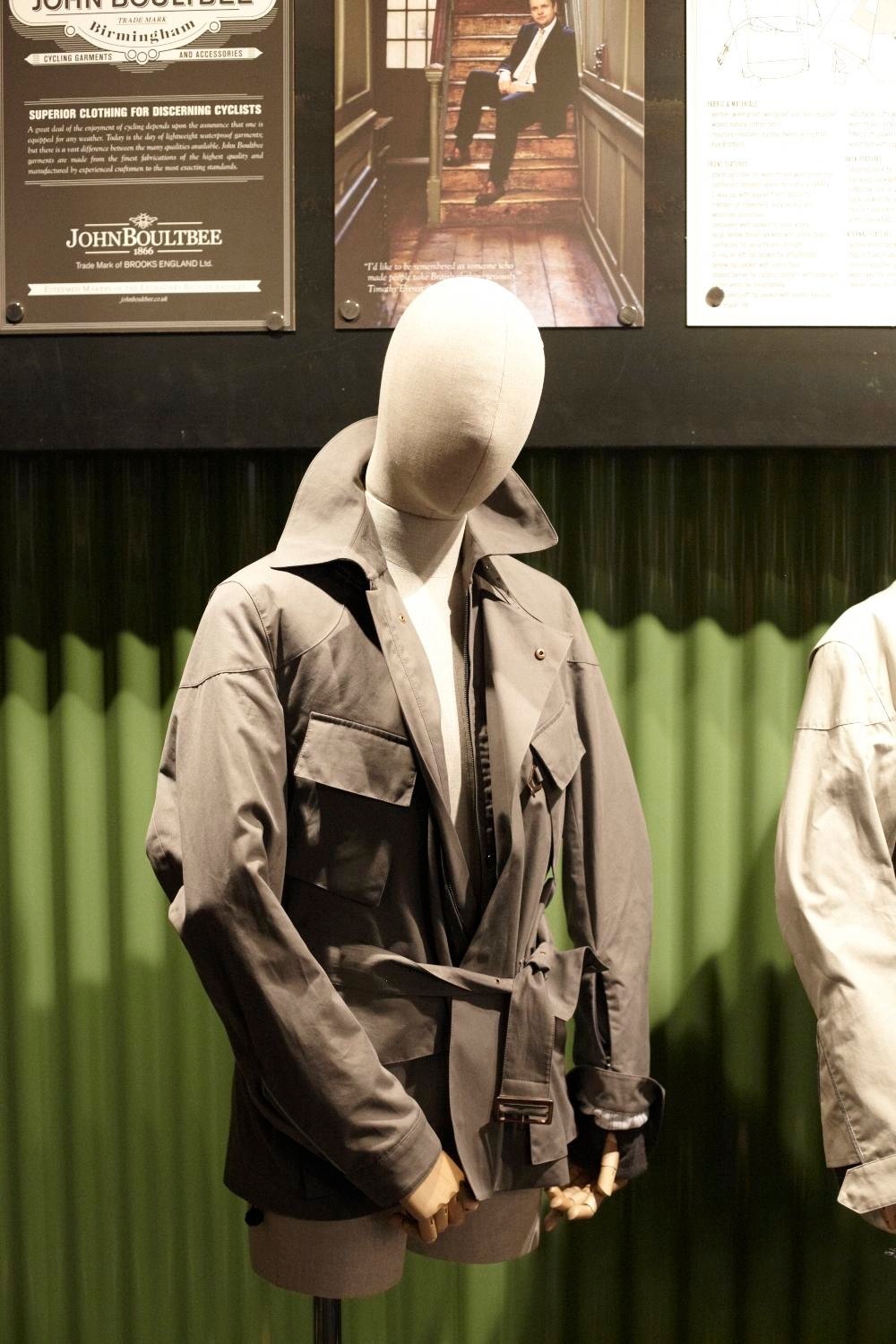 Mannequin wearing Brooks Criterion Cycling Jacket, a beige technical cycling jacket displayed against vintage John Boultbee cycling wear advertisements.