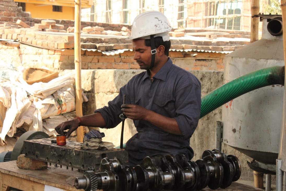 Worker in hard hat assembling industrial machinery parts at a construction site in Iraq.