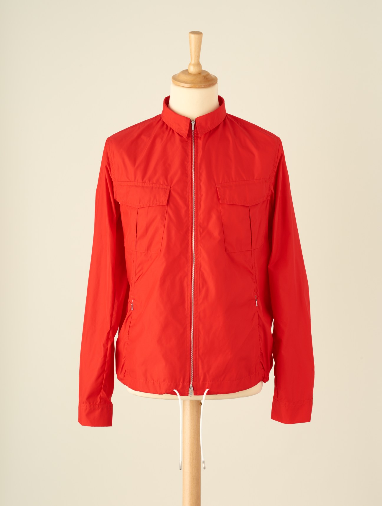 Bright red functional outdoor jacket with chest pockets and full-length zipper displayed on wooden mannequin.