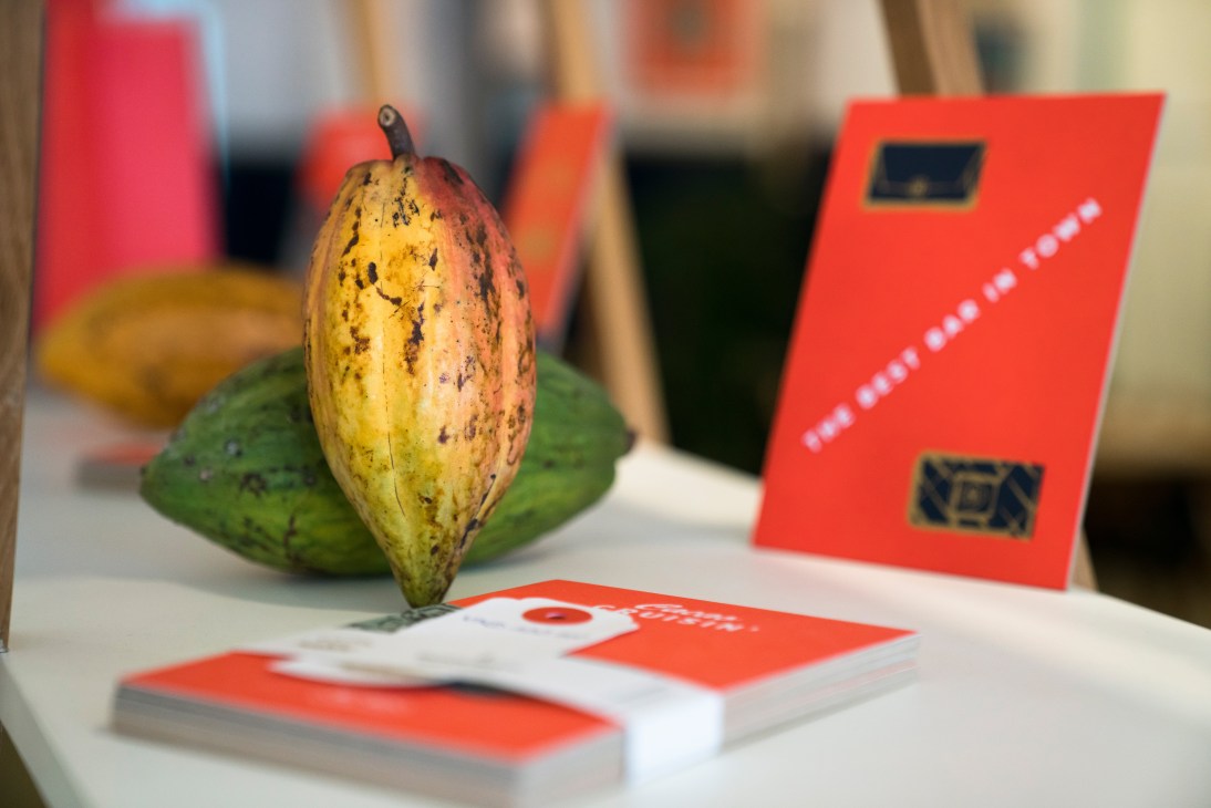 Cocoa fruit with yellow and red coloring displayed with red Marou branded cookbooks and materials.