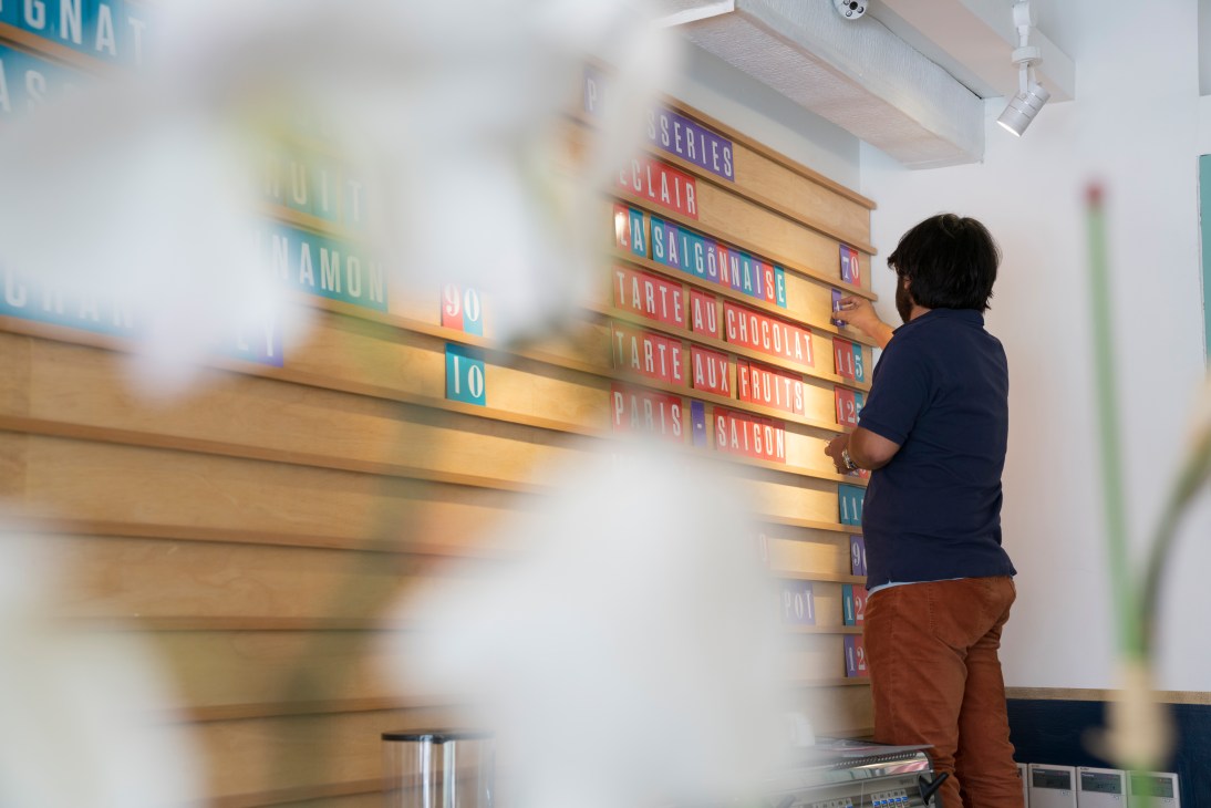Samuel Maruta adjusting colorful menu boards displaying Marou chocolate offerings at Maison Marou.