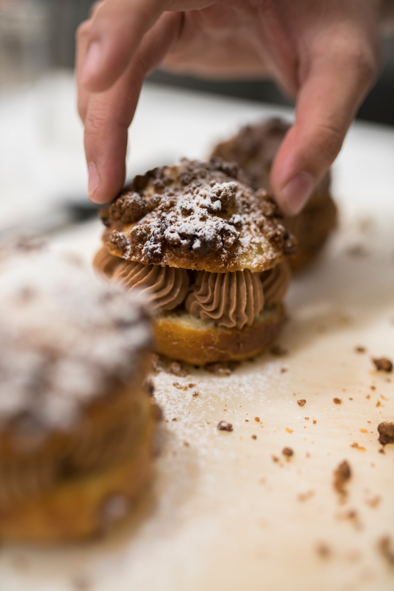 Hands holding a chocolate-dusted pastry with piped chocolate filling and cocoa powder.