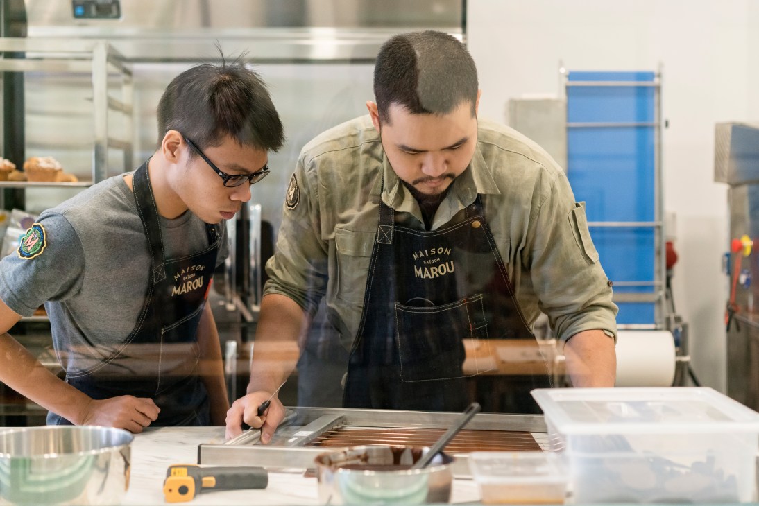 Two chefs in Maison Marou aprons prepare chocolate tuiles in the kitchen.