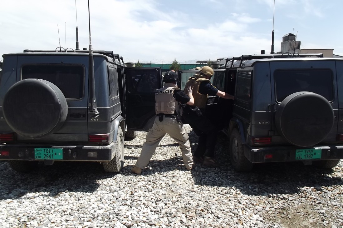 Armed security personnel in tactical gear practice defensive maneuvers between two armored vehicles during Fox Delta training.