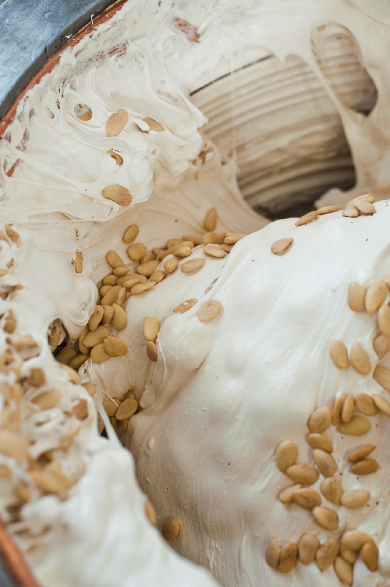 Toasted almonds being added to white nougat mixture in a large industrial mixing vessel.