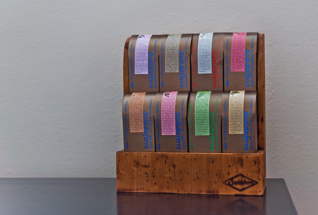 Scaldaferro nougat bars wrapped in colorful paper displayed on a wooden stand.