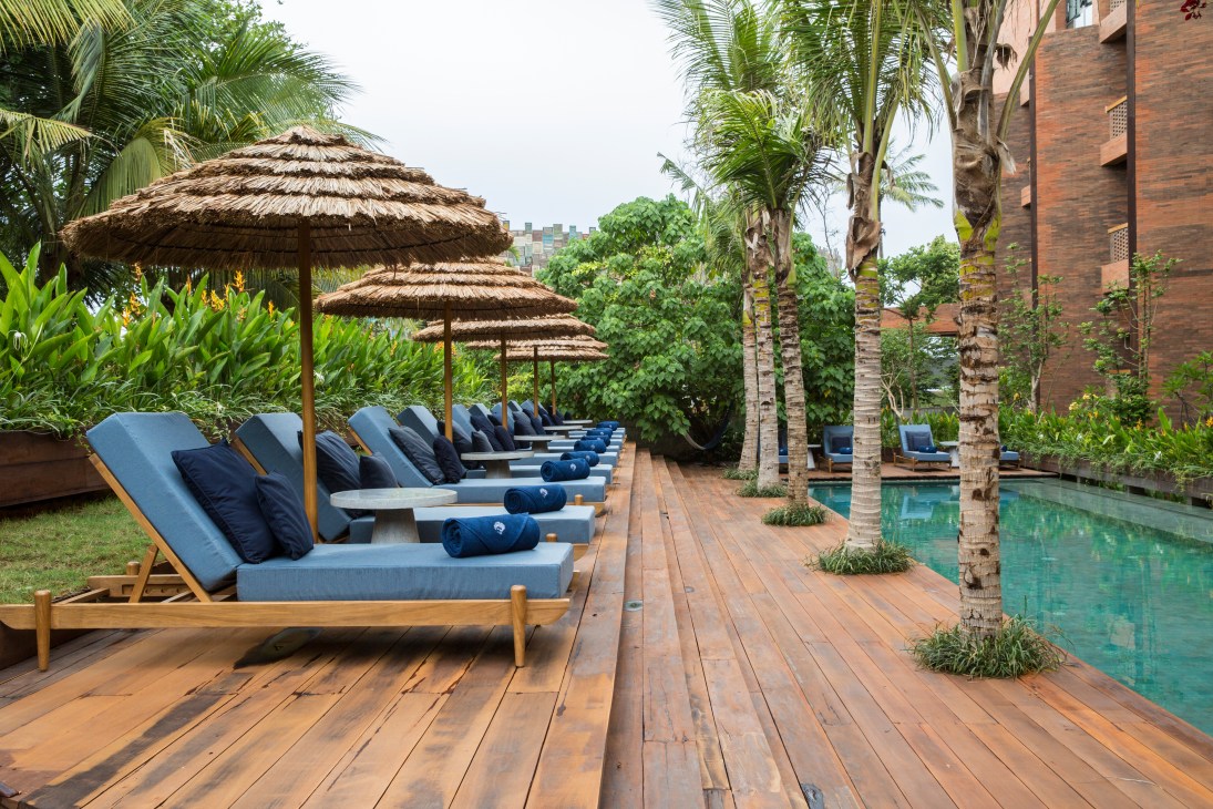 Blue lounge chairs with traditional thatched umbrellas line a wooden pool deck at Katamama hotel.