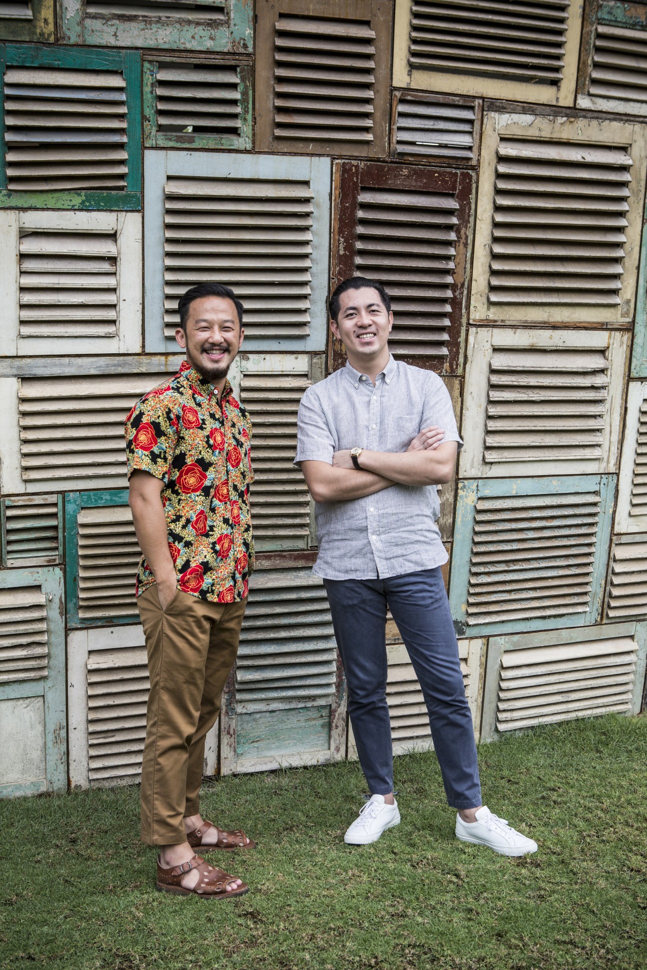Ronald Akili and Jason Gunawan, founders of PTT Family, stand smiling in front of a weathered louvered shutter wall.