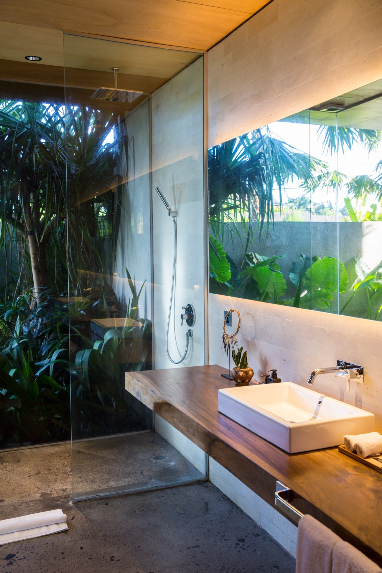 Modern bathroom at The Slow hotel with floor-to-ceiling windows overlooking tropical greenery and palm trees.