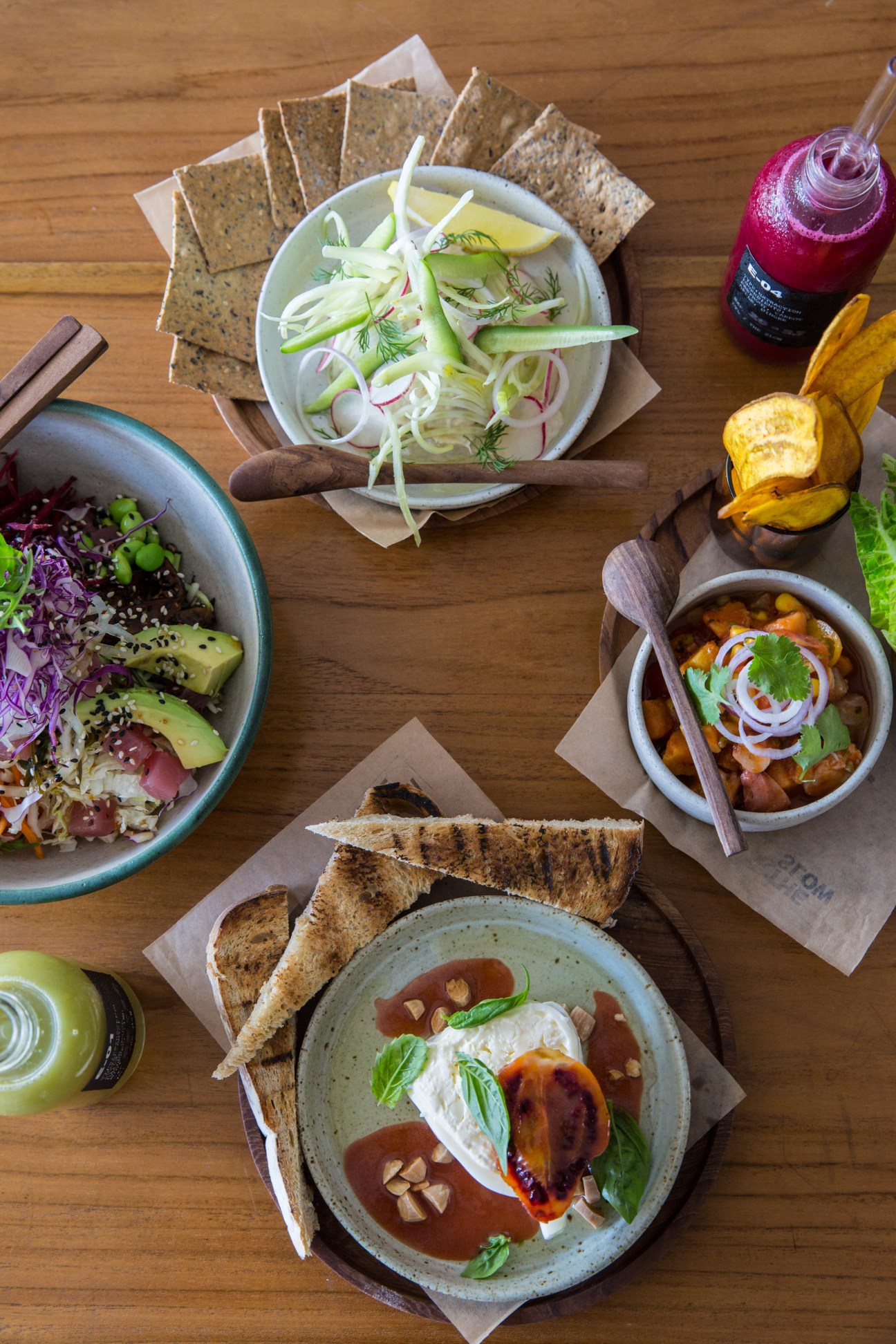 Overhead view of Indonesian dishes including salad, noodles, and grilled items on wooden table.