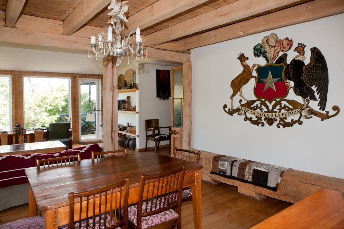Interior of Teresa Varas's restored home showing wooden beams, chandelier, dining table, and Chilean heraldic coat of arms on the wall.