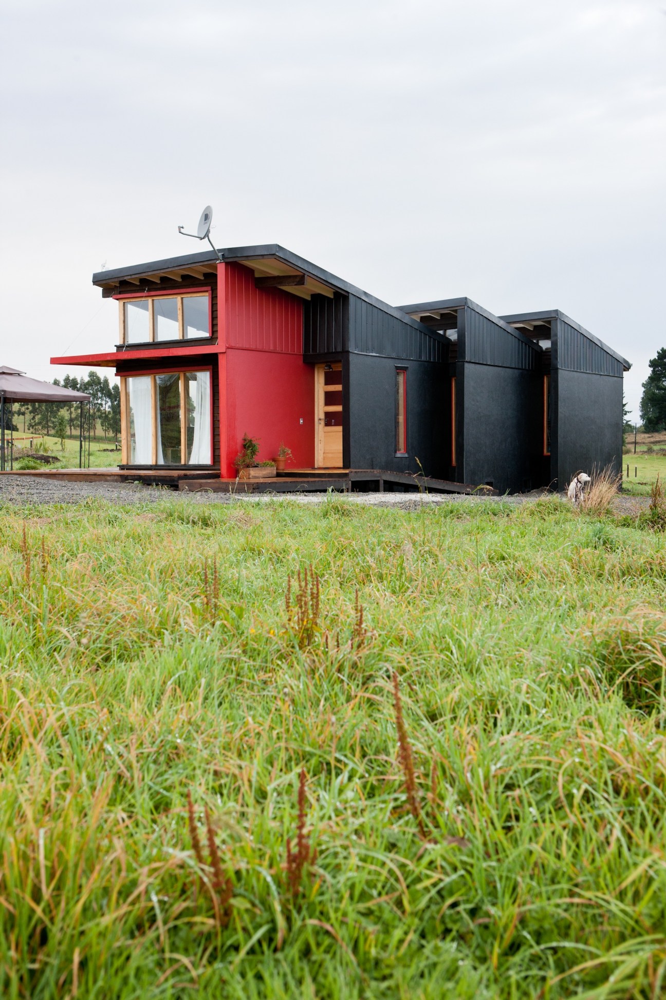 Modern eco-friendly house with red and black corrugated metal exterior in a rural setting.