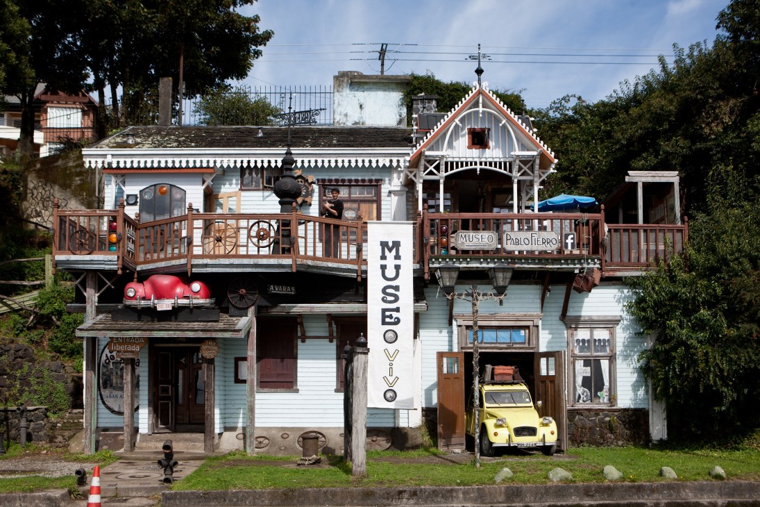 Museo Pablo Fierro, an eccentric wooden house museum with eclectic collections including a red vintage car and yellow toy car displayed outside.