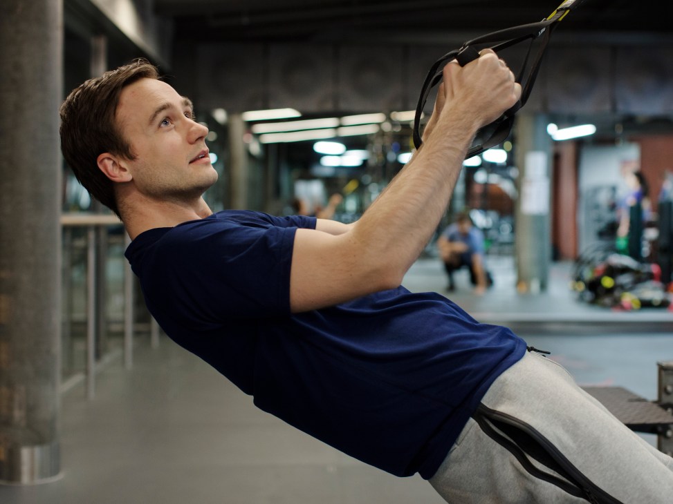 Man performing a suspension training exercise using TRX straps in a modern gym facility.