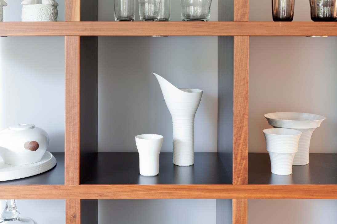 White bisque porcelain vessels displayed on wooden shelving with textured surfaces and striped details.