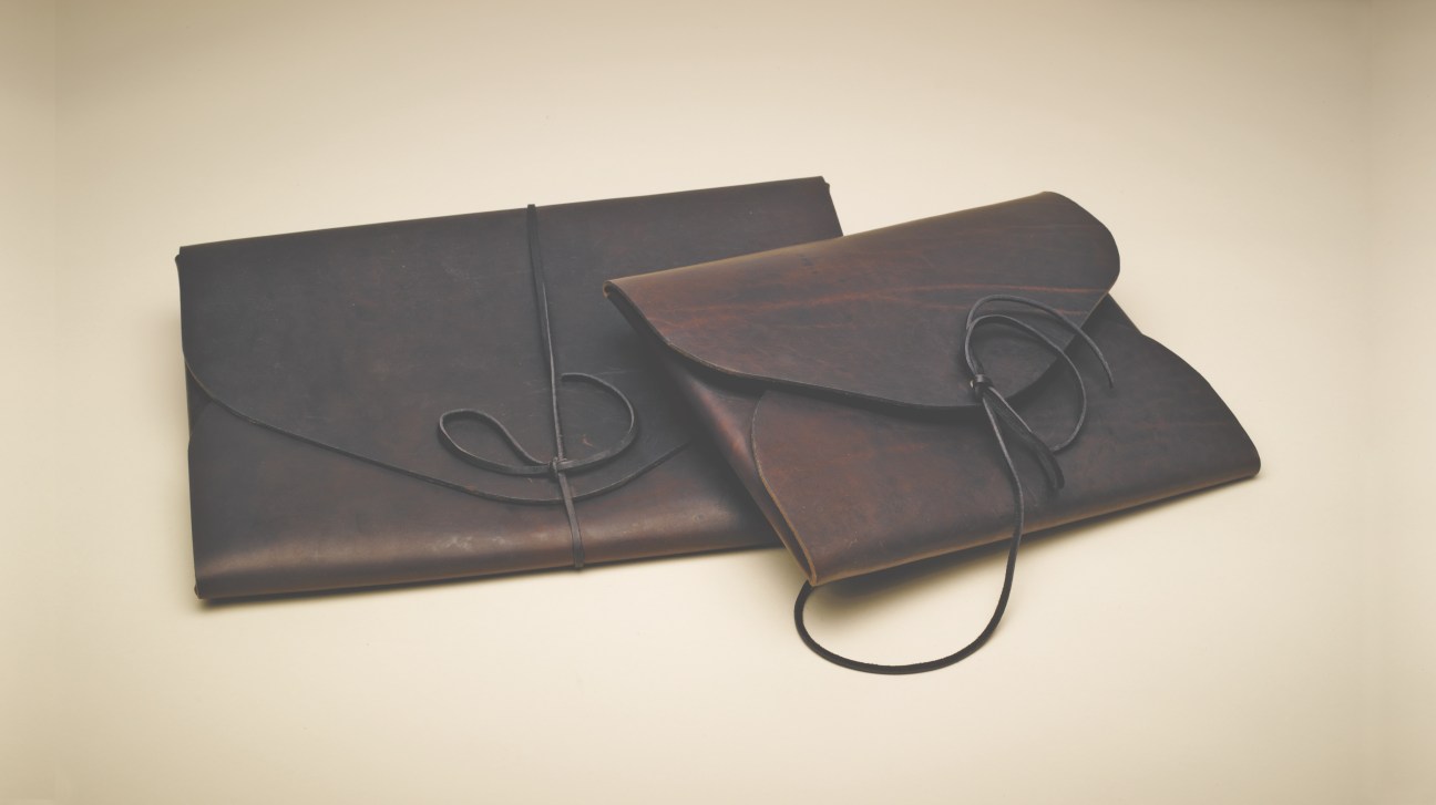 Three dark leather portfolios with copper rivets and cord closures displayed on a beige background.