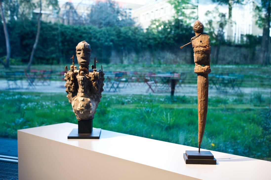 Two wooden voodoo art sculptures displayed on a white platform overlooking a garden venue.