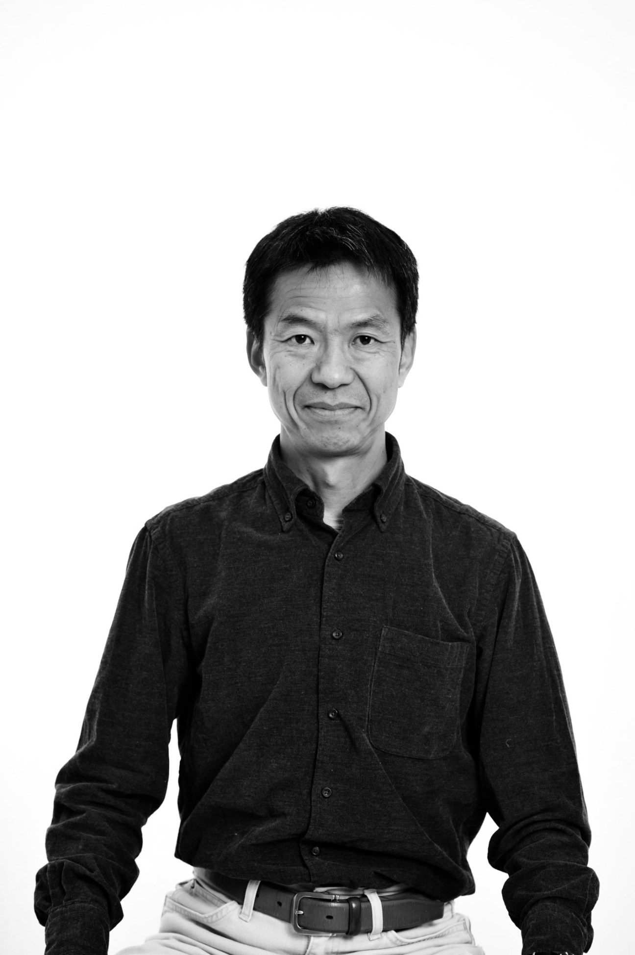 Black and white portrait of a middle-aged Asian man in a dark button-up shirt against a white background.