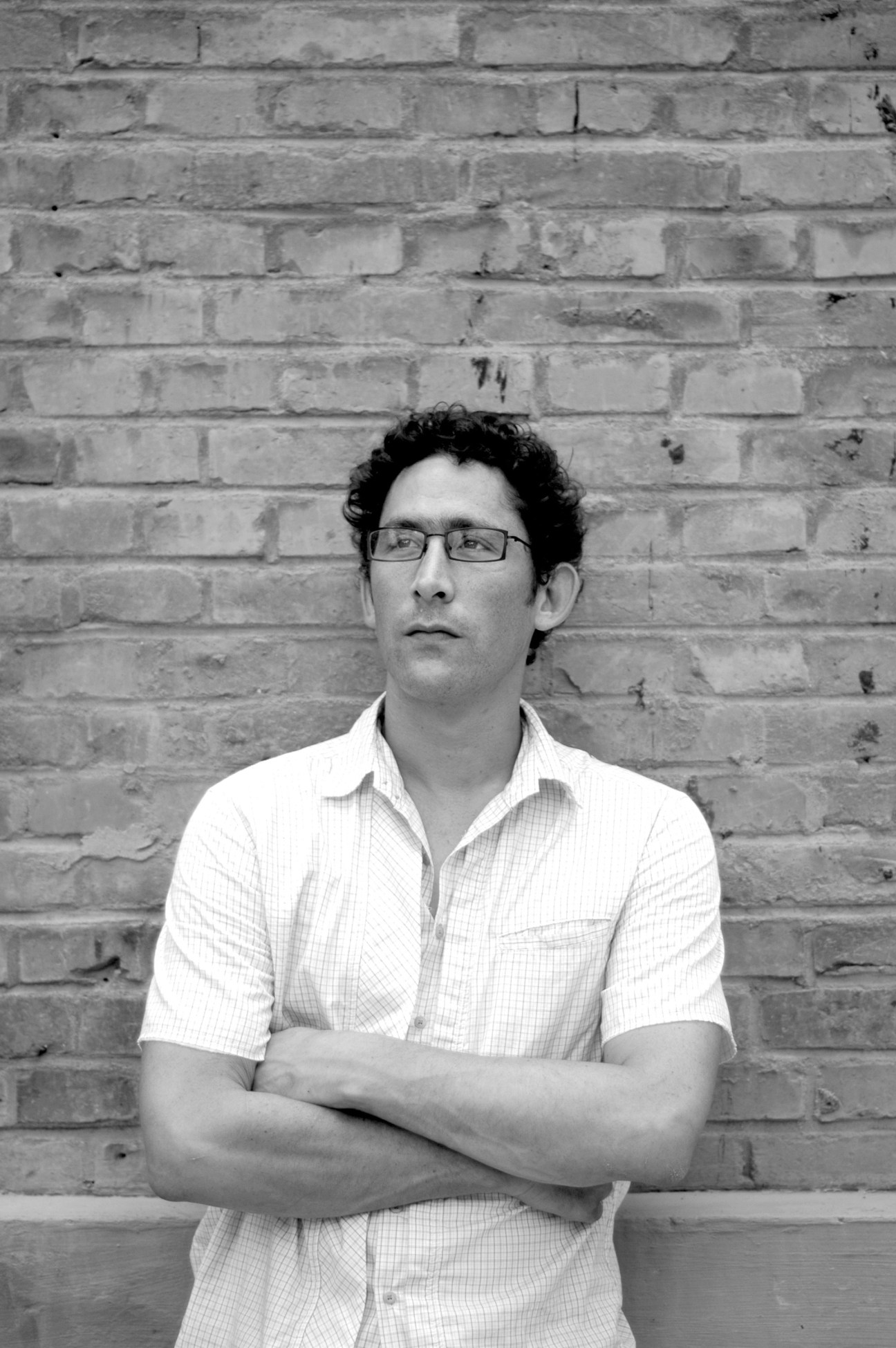 Jeremy Goldkorn, editor-in-chief of danwei.org, poses against a brick wall wearing glasses and a white shirt.