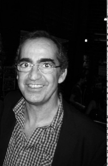 Black and white portrait photograph of Ricardo Pinto, a publisher from Macau, wearing glasses and a checkered shirt.