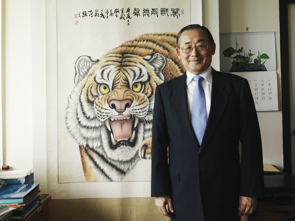 Qian Tang, assistant director-general for education, stands in an office beside a large tiger portrait.