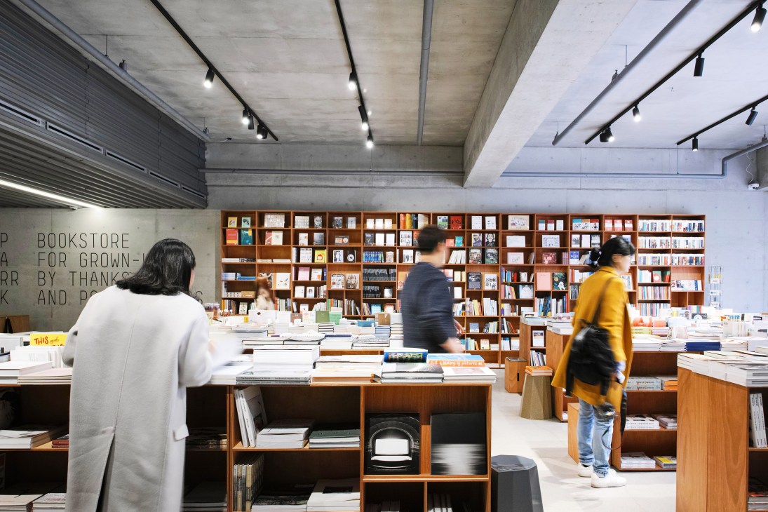 Interior of Parrk bookshop at Queenmama Market showing wooden shelving, customers browsing, and concrete ceiling with track lighting.