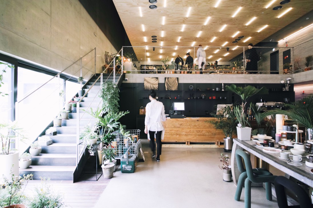Interior of Queenmama Market with wooden counter, plants, seating area, and mezzanine level with customers shopping.