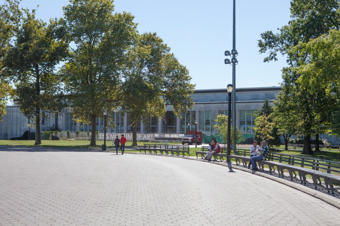 Queens Museum of Art exterior with restored entrance, park seating, and trees on a sunny day.