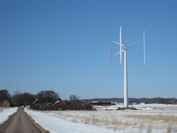 Vertical-axis wind turbine with three arms spinning silently in snowy Swedish countryside.
