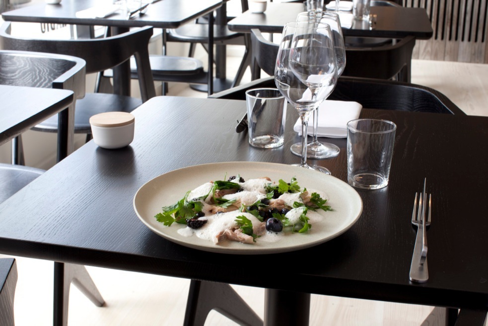 A plated dish at Radio restaurant in Copenhagen with fish, herbs and black olives on a cream plate.