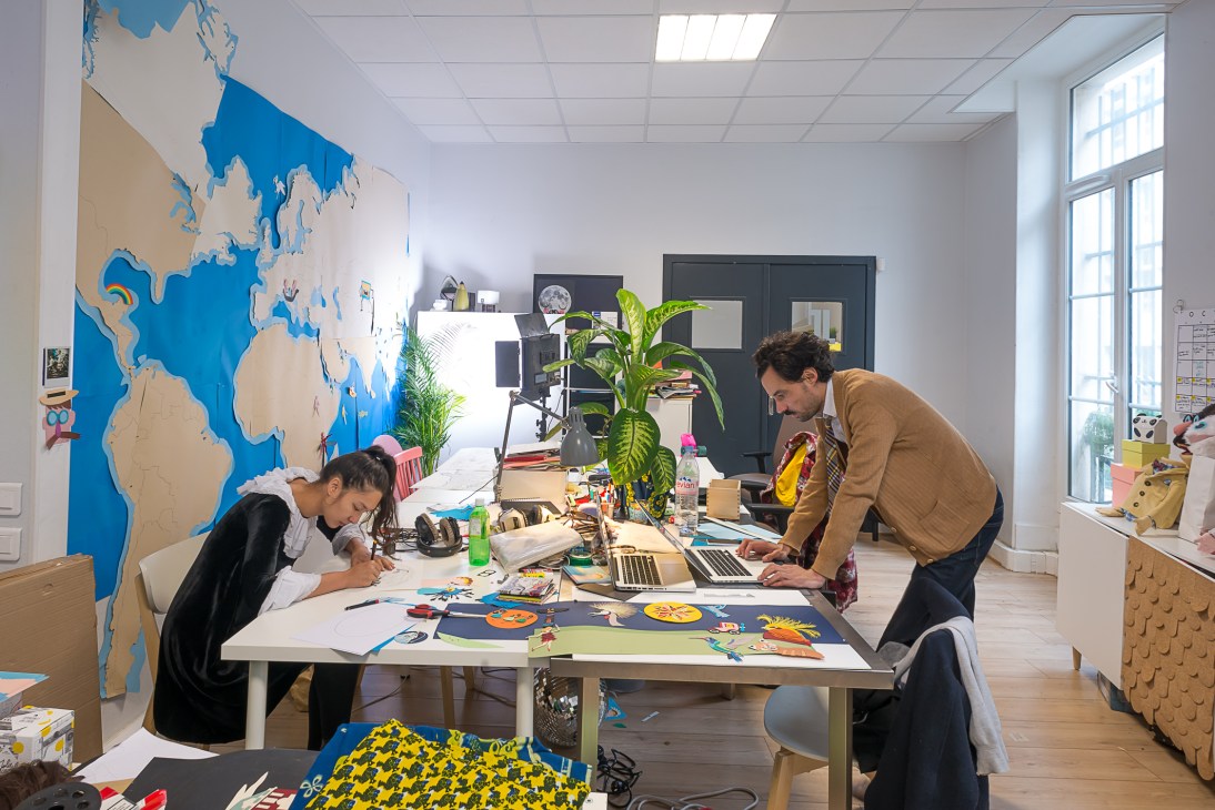 Two people working at a table in a bright office space with a large blue and beige world map on the wall.