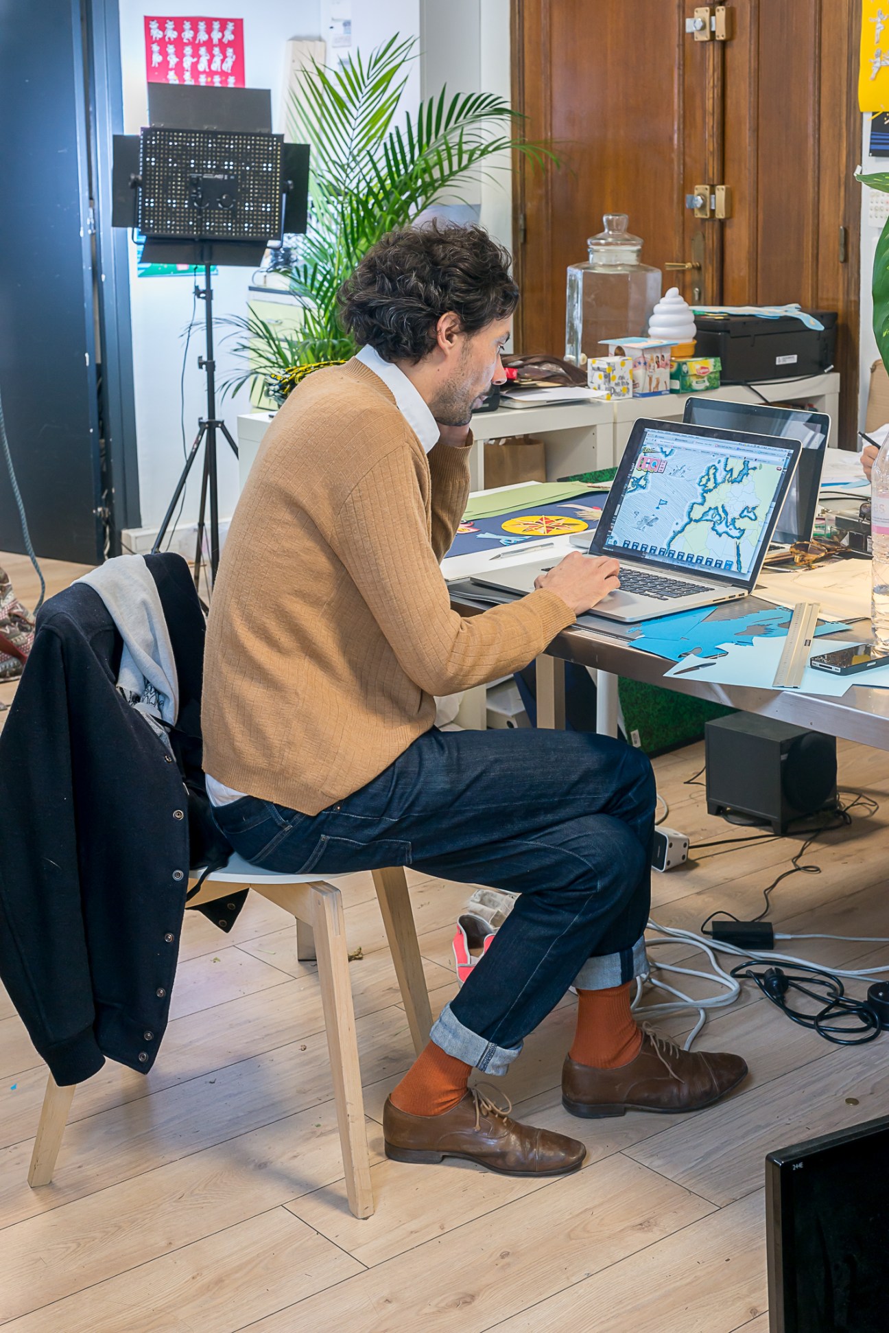 Man working at desk with laptop displaying a world map interface in a creative studio office.