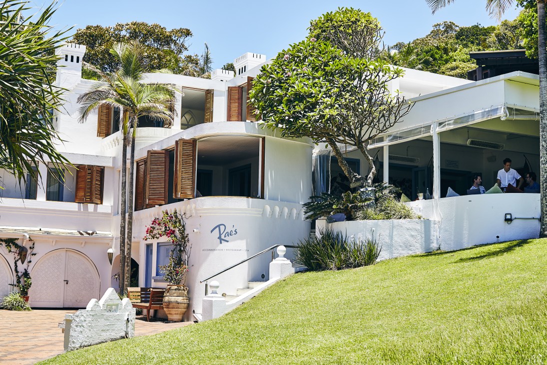 Rae's restaurant, a white modernist building on Wategos Beach with tropical plants and ocean views.