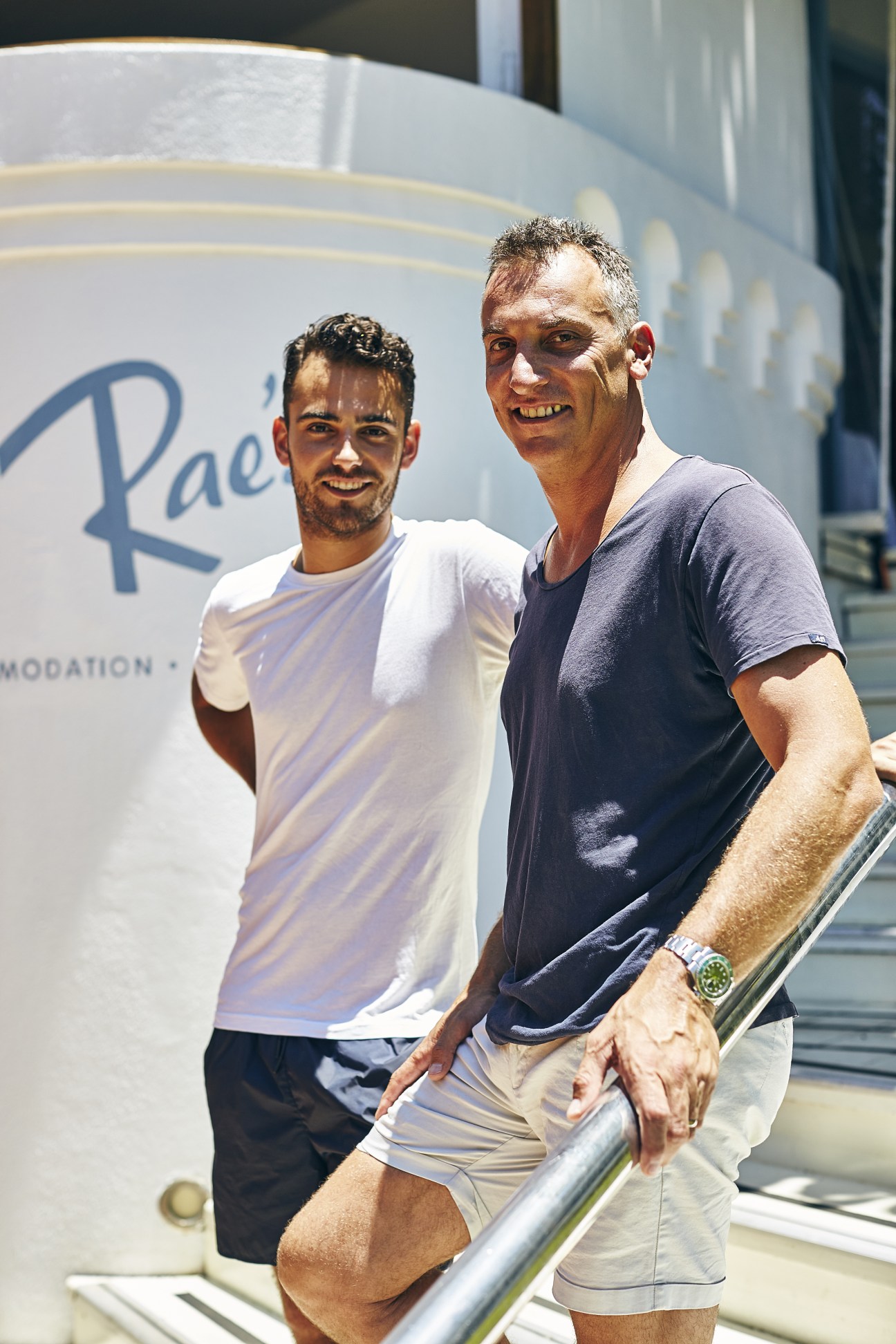 Two men smile outside Rae's restaurant on Wategos Beach in Byron Bay.