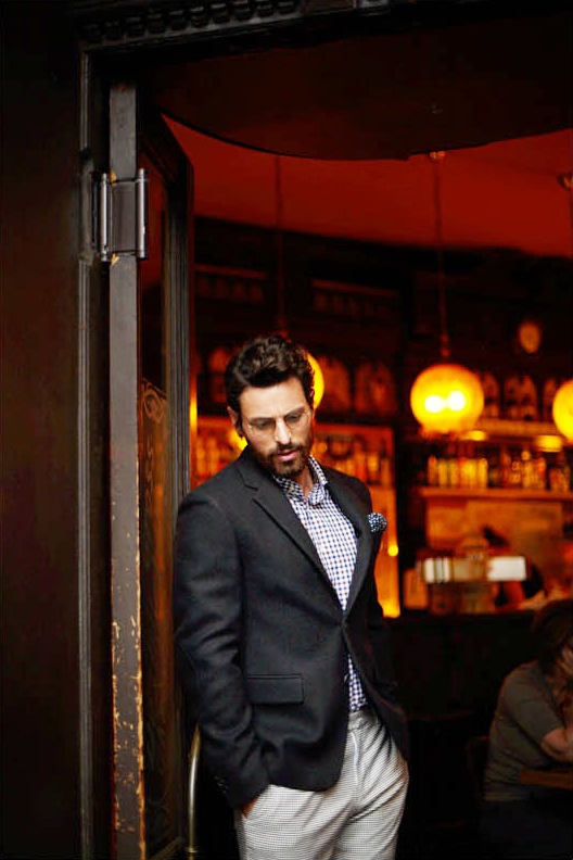 Man in Prada jacket and Danolis shirt standing at bar entrance with warm interior lighting