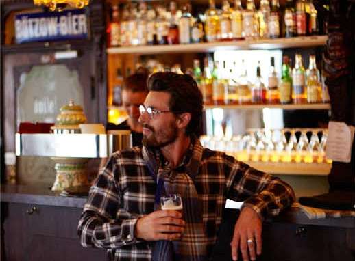 Model Nikolaij Schulz seated at a Berlin bar counter wearing Franco Bassi shirt and United Arrows trousers.