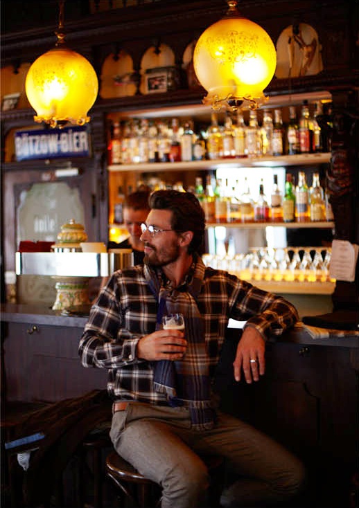 Model Nikolaij Schulz seated at a Berlin bar counter wearing Franco Bassi shirt and United Arrows trousers.