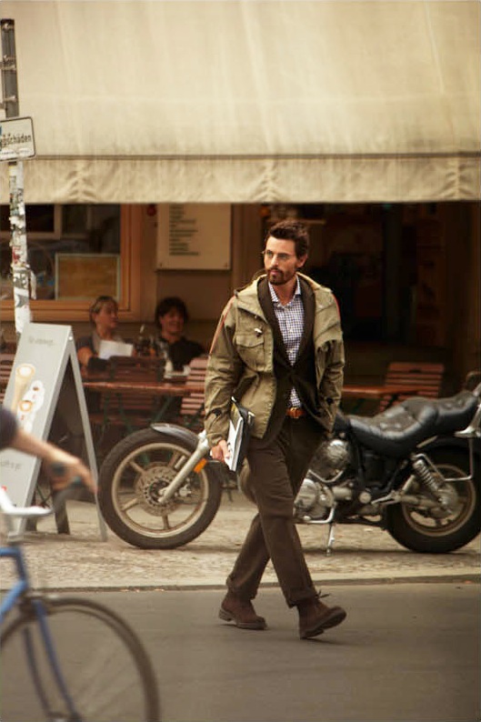 Model Nikolaij Schulz walks past a Berlin bar wearing RLX Ralph Lauren coat, Bally jacket and trousers, and Mykita glasses.