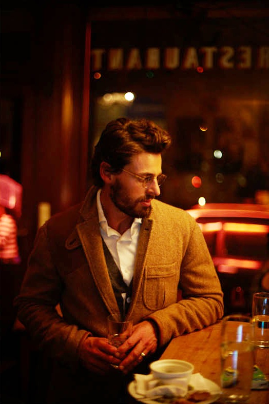Man wearing Ralph Lauren jacket and Sacai cardigan sits at a Berlin bar table.