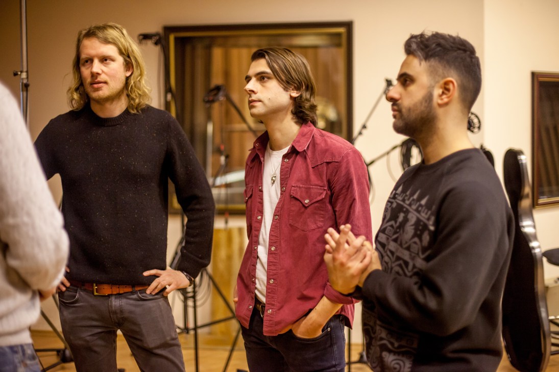 Three young male musicians from British band Rale stand in a studio, discussing their upcoming recording session with the Czech National Symphony Orchestra.