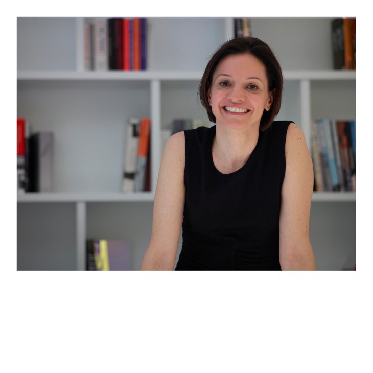 Woman smiling at camera in front of white shelving unit filled with books