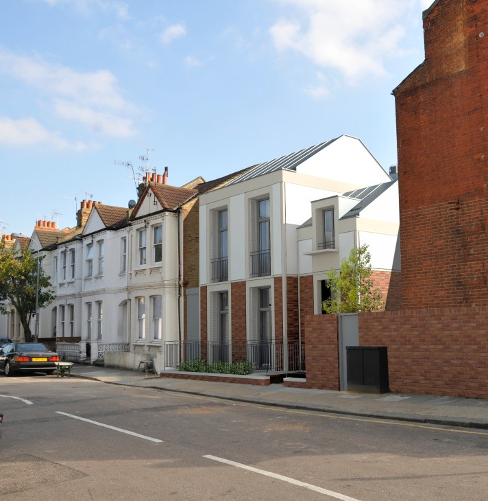 Modern white townhouse with brick base nestled between traditional Victorian properties on a London street.