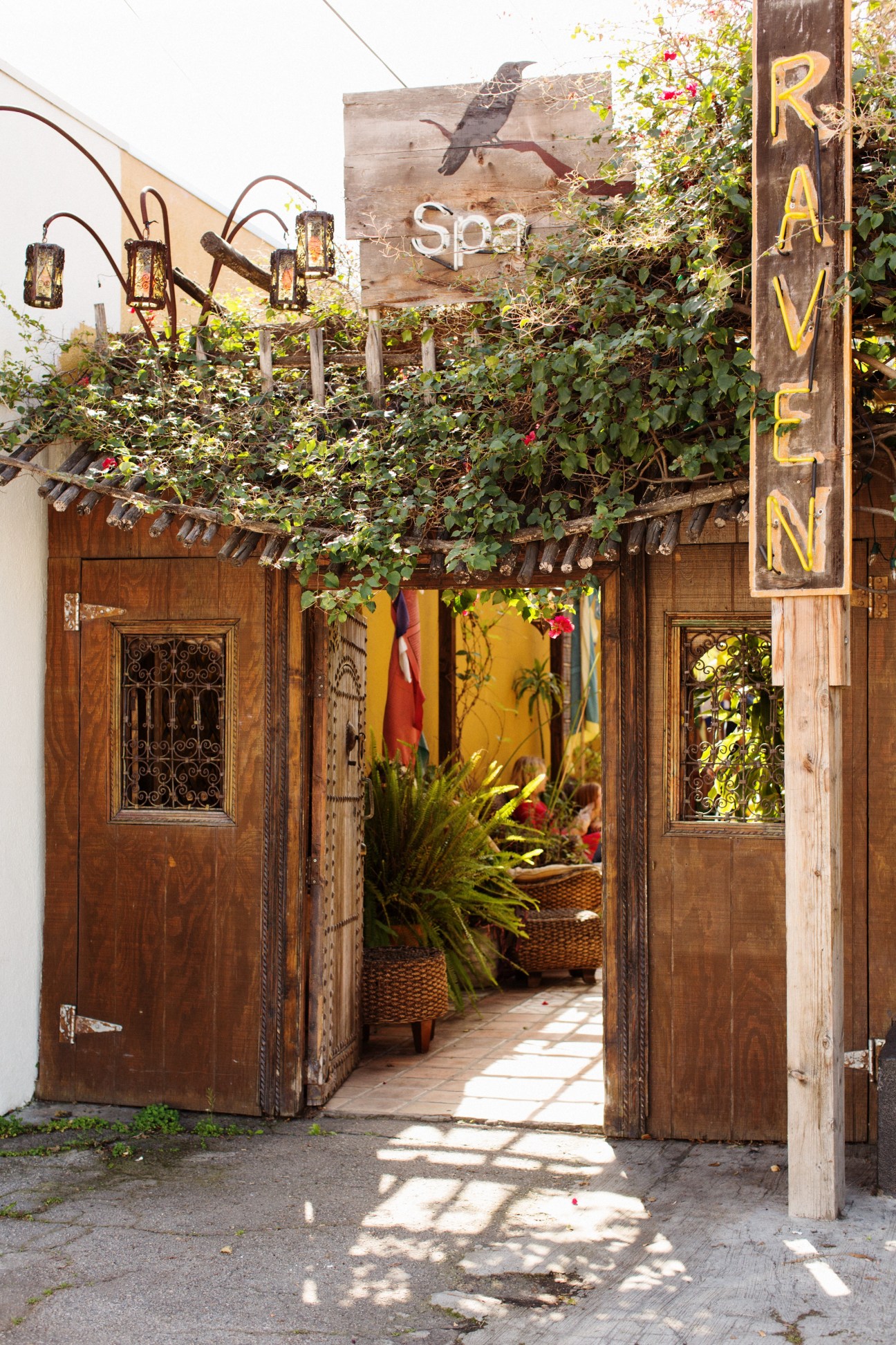 The Raven Spa entrance with wooden doors, ivy-covered pergola, and decorative lanterns.