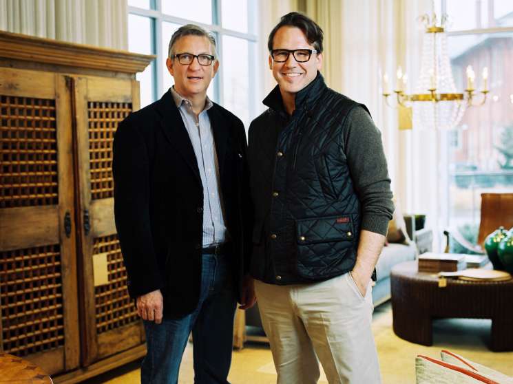 Billy Woodall and Rodney Simmons standing in an upscale interior with vintage wooden cabinetry and large windows.