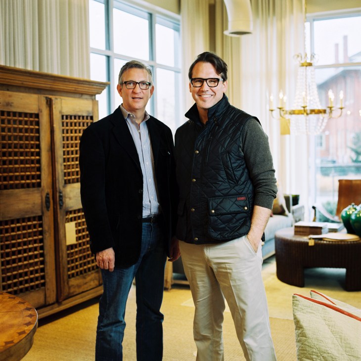 Billy Woodall and Rodney Simmons standing in an upscale interior with vintage wooden cabinetry and large windows.